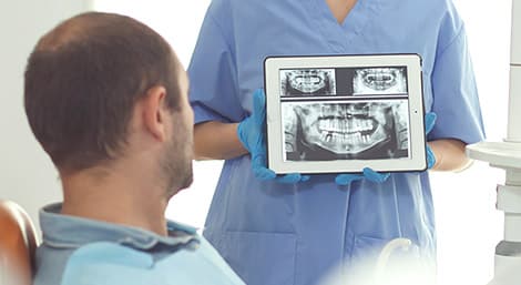 Dentist in blue scrubs showing dental X-rays to patient in clinical setting.
