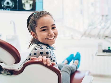 Young girl in dental chair wearing bib, smiling during dental examination in clinic.
