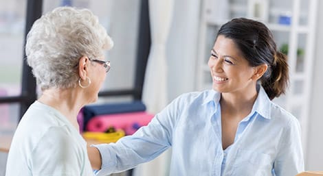 Caregiver and elderly woman smiling while having a conversation in a bright, modern clinical setting.