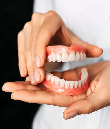 Hands displaying a full set of dental implants or dentures against a dark background.
