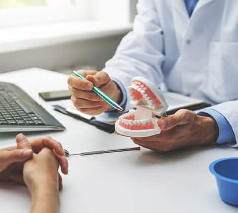 Dentist showing patient dental model during consultation at office desk with laptop