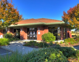 Modern brick dental office building with autumn foliage and landscaped front garden under clear blue sky.