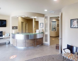 Modern dental office reception area with curved desk, seating area, and clinical spaces visible in background.