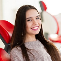 Smiling woman with long dark hair in dental office with red decorative elements in background