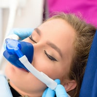 Young patient receiving dental treatment with blue gloves and protective mask in clinical setting.