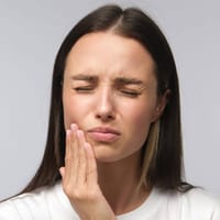 Woman touching cheek with pained expression, indicating dental discomfort or toothache.