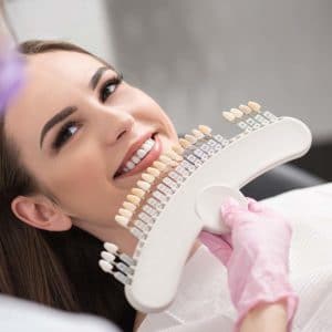 Woman receiving professional teeth whitening treatment with LED device at dental clinic.