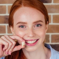 Young woman with red hair smiling brightly while holding dental floss against brick background.