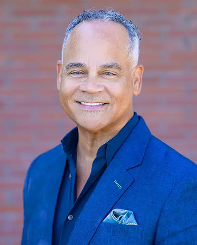 Professional headshot of smiling man in blue blazer against brick background for dental practice.