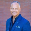 Professional headshot of male dentist wearing blue Pure Dentistry polo shirt against brick background.