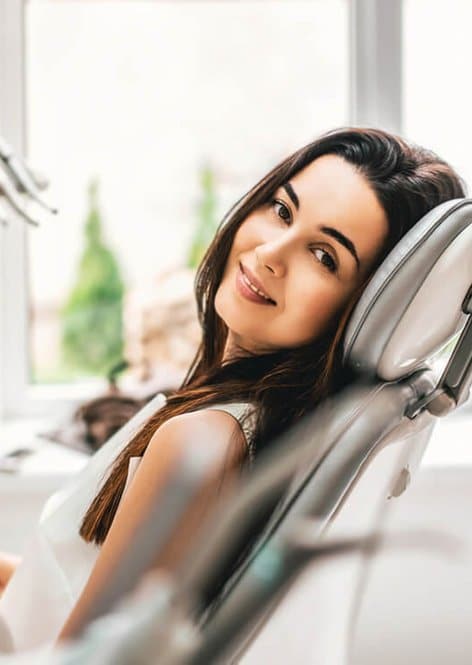 Smiling woman relaxing in dental chair at modern dentistry clinic.