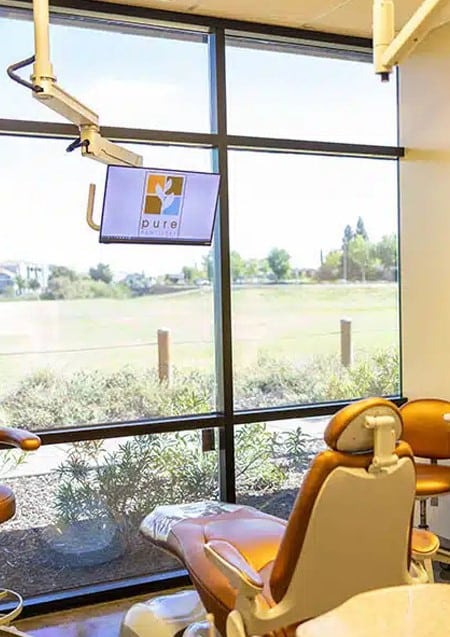 Dental office interior with chair overlooking pastoral landscape through large windows.