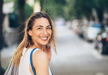 Smiling woman with healthy teeth outdoors on a sunny street, looking back at camera.